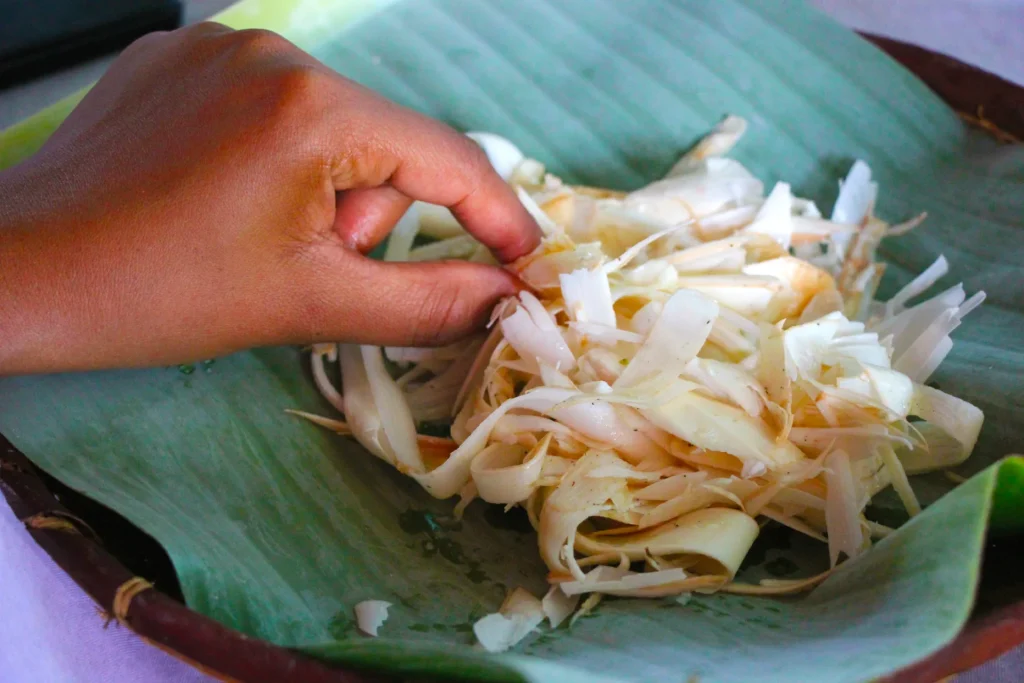 Hand of a woman taking palm kernel salad from a banana leaf.